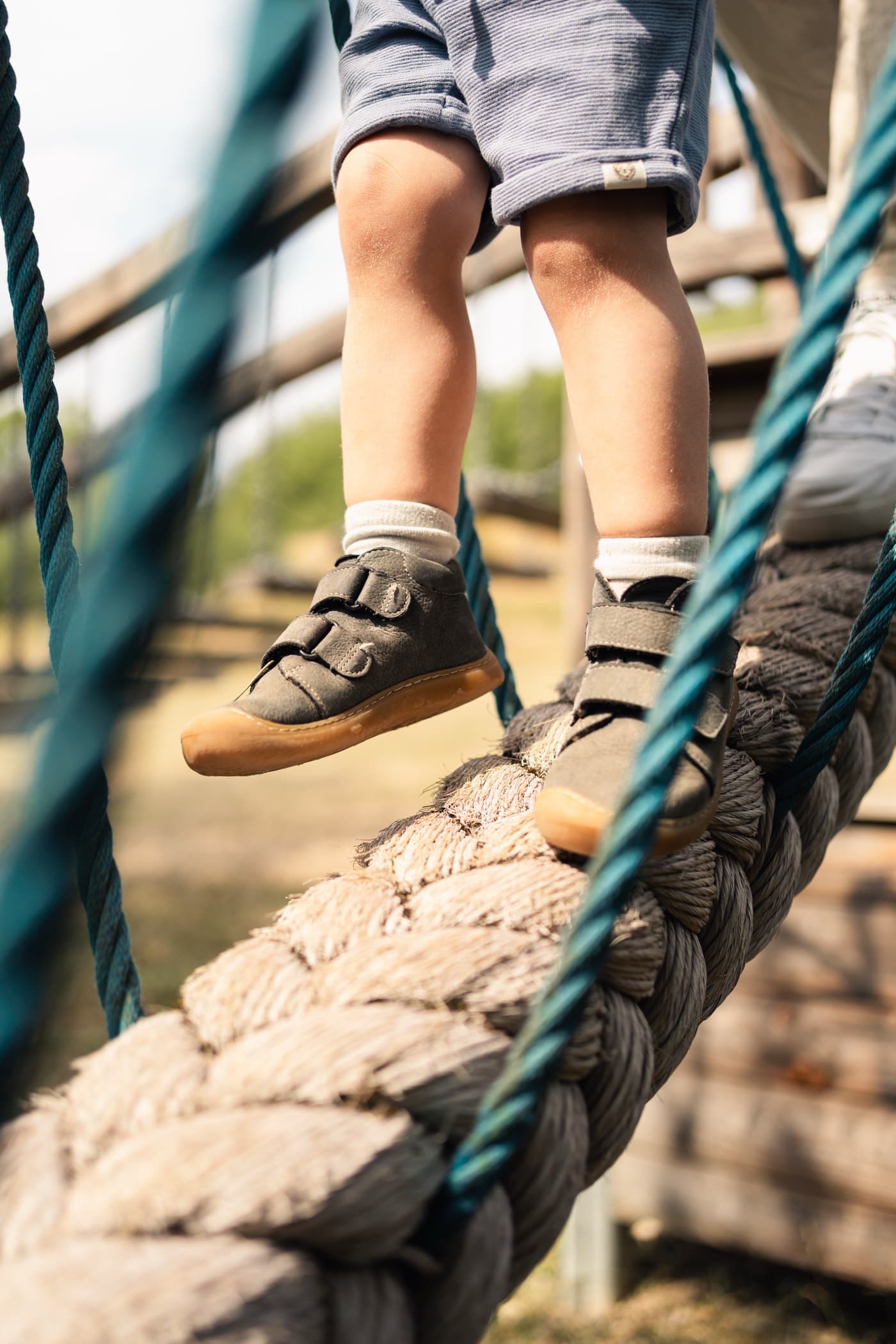 Kinderbeine balancieren über eine Seilbrücke auf dem Spielplatz